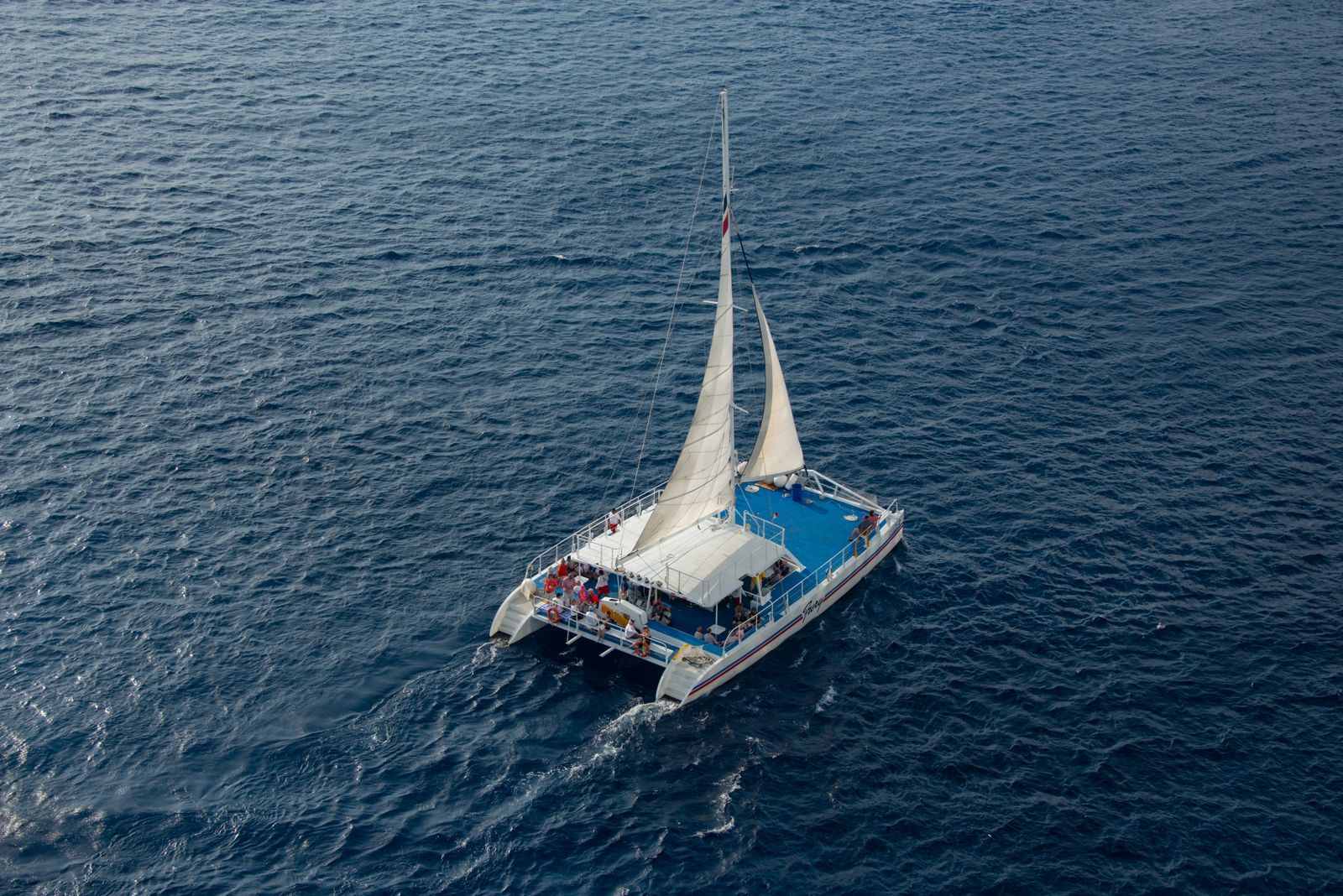 Aerial view of a sailing catamaran with passengers on deep blue water, like a Molokini snorkel tour boat from Maui